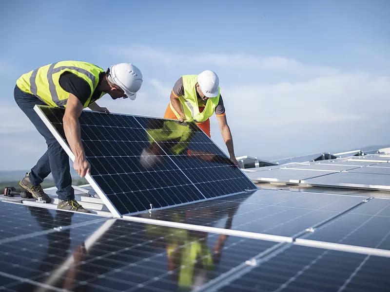 Zwei Monteure in Warnwesten und Schutzhelmen installieren Photovoltaikmodule