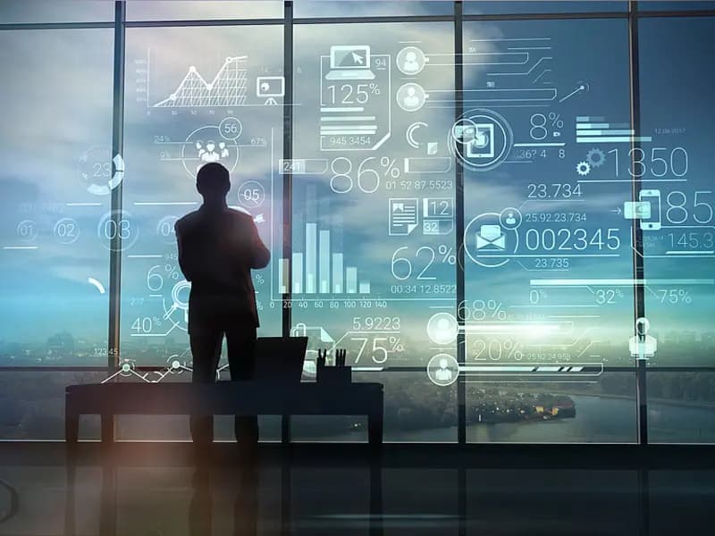 Silhouette eines Mannes vor einer Glasfront mit eingeblendeten Finanzdaten und Diagrammen